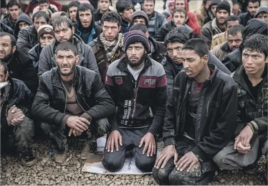  ?? Photograph­s by Marcus Yam Los Angeles Times ?? MEN KNEEL silently, waiting for their names to be called by community police for their security screening at the camp in Hamam Alil, Iraq.