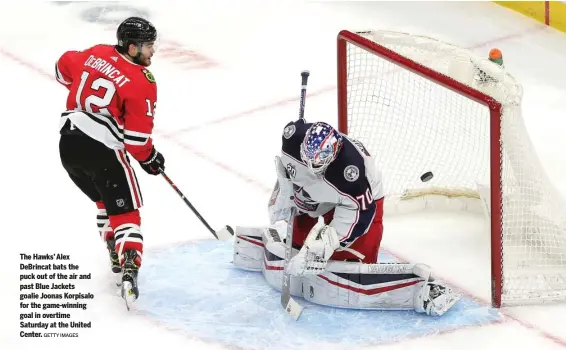  ?? GETTY IMAGES ?? The Hawks’ Alex DeBrincat bats the puck out of the air and past Blue Jackets goalie Joonas Korpisalo for the game-winning goal in overtime Saturday at the United Center.