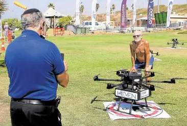  ?? ?? ONE MORE FAN A man poses next to a drone set up to deliver cargo along with two other unmanned aerial vehicles in a delivery simulation. Two of the drones carried sushi while the third had beer.