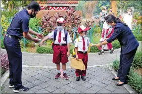  ??  ?? Staff members check body temperatur­es of students Monday on the first day of school reopening in Jakarta.