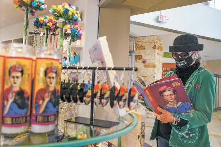  ?? PHOTOS BY GABRIELA CAMPOS/THE NEW MEXICAN ?? Jo Owen looks through a Frida Kahlo art book while surrounded by wares bearing the artist’s face at the Albuquerqu­e Museum, where Frida Kahlo, Diego Rivera and Mexican Modernism is on exhibit.