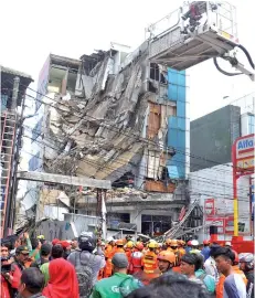  ?? — AFP photo ?? A crowd gathers to watch rescuers as they search a five-storey building after part of the structure collapsed in Jakarta.