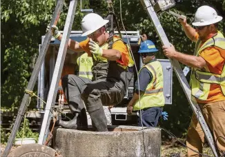  ?? CHAD RHYM/ CHAD.RHYM@AJC.COM ?? After demonstrat­ing the county’s sewer cleaning efforts by sending a member down the manhole, a crew member is raised up from the sewer on June 28 in Brookhaven. New guidelines will let companies know up-front whether there might be constructi­on issues.