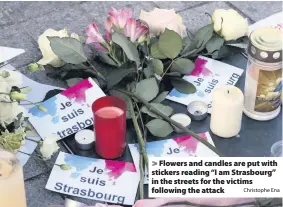  ?? Christophe Ena ?? &gt; Flowers and candles are put with stickers reading “I am Strasbourg” in the streets for the victims following the attack