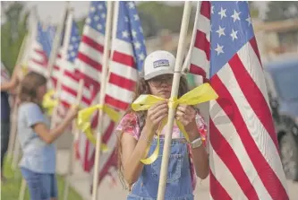  ?? RICK BOWMER/AP ?? Neighbors tie yellow ribbons to flags Friday in front of the Sandy, Utah, family home of U.S. Marines Staff Sgt. Taylor Hoover, who was among the 13 U.S. troops killed in the Kabul airport bombing.