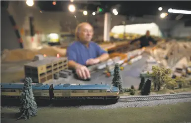  ?? Photos by Paul Chinn / The Chronicle ?? An HO scale train rolls past Wayne Monger while he cleans a section of track at the model railroad layout.