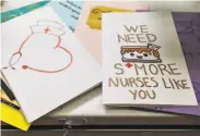  ??  ?? Left: Nurse Kristen Tritt shows the protective hood of her powered airpurifyi­ng respirator. Right: A stack of colorful thankyou cards sits at the nurses’ station in the fifthfloor COVID unit.