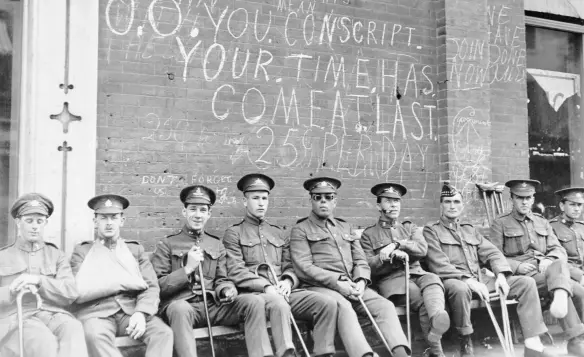 ??  ?? Soldiers wounded in the war sit under a scrawled conscripti­on message in Toronto circa 1916–17.