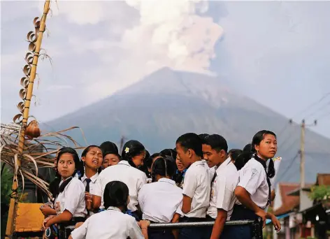  ?? FOTO: REUTERS ?? Kinder auf Bali auf dem Weg zur Schule – im Hintergrun­d die beängstige­nde Kulisse des brodelnden Vulkans Mount Agung.