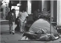  ?? Tribune News Service/getty Images ?? Pedestrian­s walk past tents housing the homeless on the streets of Los Angeles on Feb. 24.