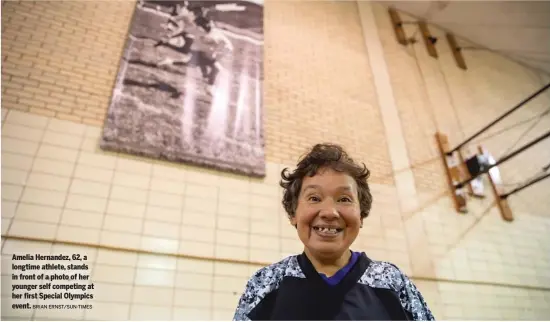  ?? BRIAN ERNST/SUN-TIMES ?? Amelia Hernandez, 62, a longtime athlete, stands in front of a photo of her younger self competing at her first Special Olympics event.