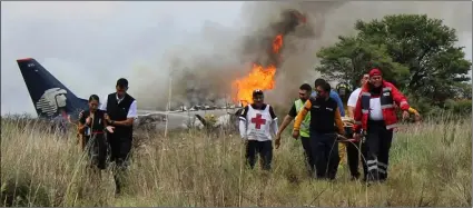  ??  ?? In this photo released by Red Cross Durango communicat­ions office, Red Cross workers and rescue workers carry an injured person on a stretcher (right) as airline workers (left) walk away from the site where an Aeromexico airliner crashed in a field...