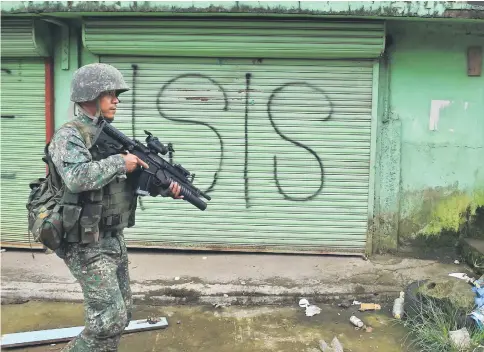  ??  ?? A Philippine Marine walks past graffiti during a patrol along a deserted street at the frontline in Marawi, on the southern island of Mindanao. — AFP photo
