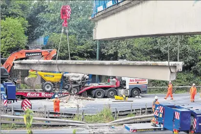  ??  ?? Cranes lift the collapsed section of the footbridge from the M20 roadway on to a transporte­r lorry yesterday