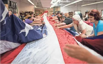  ?? TYGER WILLIAMS / MILWAUKEE JOURNAL SENTINEL ?? Eder Flag Manufactur­ing Co. workers gather to help clean and fold a 30-by-60-foot flag made by the Oak Creek firm and purchased by an Army unit. The flag was damaged at Bagram Airfield in Afghanista­n, and the Eder employees repaired it before returning it to the unit this week. More photos at jsonline.com/news.