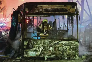  ?? Avshalom Sassoni / Associated Press ?? An Israeli firefighte­r extinguish­es a burning bus Tuesday after it was hit by a rocket fired from Hamas-controlled Gaza Strip, at the central Israeli town of Holon, near Tel Aviv.