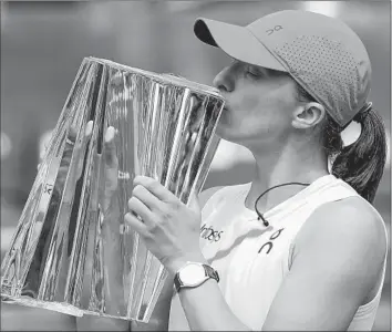  ?? Ryan Sun Associated Press ?? IGA SWIATEK of Poland kisses the trophy after she defeated Maria Sakkari of Greece in the women’s final of the BNP Paribas Open. Swiatek lost just 21 games in her six matches over the 12-day tournament.