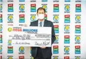  ?? MICHIGAN LOTTERY VIA AP ?? Attorney Kurt Panouses poses with a check on behalf of the winners of a Mega Millions lottery jackpot.