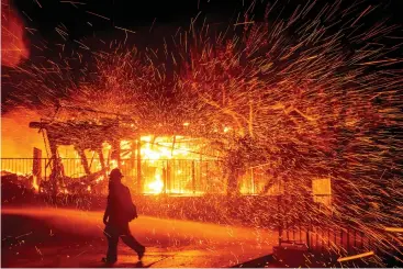  ?? Associated Press ?? ■ A firefighte­r passes a burning home Thursday as the Hillside fire burns in San Bernardino, Calif.