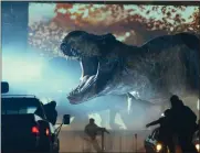  ?? AP ?? A dinosaur steps in front of the screen at a drive-in movie theater in a scene from ‘Jurassic World: Dominion.’