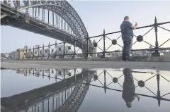  ?? BLOOMBERG ?? A man takes a photograph near the Sydney Harbour Bridge in Sydney as Australia reduces restrictio­ns due to cases falling.