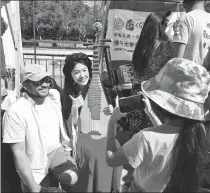  ?? PROVIDED TO CHINA DAILY ?? Wang Yijun, holding her pipa, poses for pictures with a resident in front of the Tsinghua booth at the Joyful Spring Festival event in the Santiago Sculpture Park in Chile.