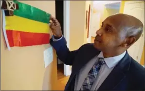  ?? (AP/Allen G. Breed) ?? Tewodrose Tirfe stretches out a small Ethiopian flag displayed in the family room of his home Oct. 21 in Harrisburg, N.C. Tirfe is chairman of the Amhara Associatio­n of America, an advocacy group for Ethiopia’s second-largest ethnic group.