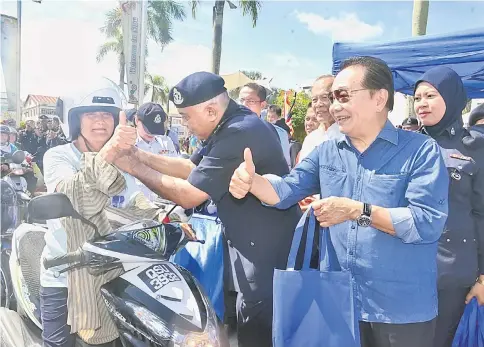  ??  ?? Azman (front, second right) helps a motorcycli­st fasten her new crash helmet as Wong (front, right) and others look on.