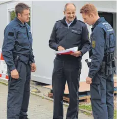  ?? FOTO: TANJA BOSCH ?? Polizeidir­ektor Guido Mebold (Mitte) steht mit den zwei Polizeimei­steranwärt­ern Alexander Richter (links) und Daniel Fritz vor den neuen Bürocontai­nern für die Lehrer und zeigt ihnen die Pläne.