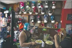  ??  ?? Lucha Libre brothers “Ciclonico” (left) and Mister Jerry eat at their restaurant that also sells fighter masks in Xochimilco. While wrestling halls are closed amid the covid-19 pandemic, they now make their livings selling flowers they grow on Xochimilco’s artificial islands, known as chinampas, and selling tacos and tortas.