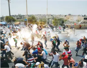  ?? (Ammar Awad/Reuters) ?? PALESTINIA­NS RUN from tear gas fired by police after prayers turned into a riot outside Jerusalem’s Old City on Friday.