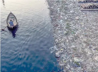  ?? — AFP photo ?? File photo shows a man paddles on a boat as plastic bags float on the water surface of the Buriganga river in Dhaka.