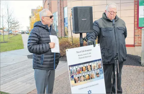  ?? KATHERINE HUNT/THE GUARDIAN ?? Speaker George Gilliland, a retired Chaplin at the Queen Elizabeth Hospital, points to the photos of the victims of the Pittsburgh synagogue attack during the vigil held at Founder’s Hall on Sunday. On the left is P.E.I. Jewish Community president Leo Mednick.