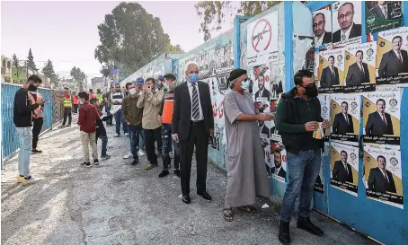  ?? AFP ?? Voters wearing masks as a precaution against COVID-19 queue outside a polling station to vote at Al-Baqaa camp for Palestinia­n refugees, north of Amman.