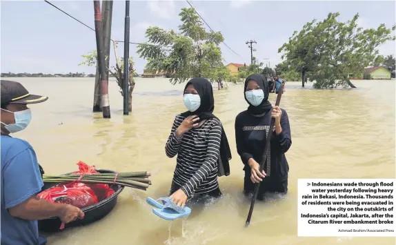  ?? Achmad Ibrahim/Associated Press ?? Indonesian­s wade through flood water yesterday following heavy rain in Bekasi, Indonesia. Thousands of residents were being evacuated in
the city on the outskirts of Indonesia’s capital, Jakarta, after the
Citarum River embankment broke