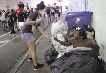  ?? Gary Coronado Los Angeles Times ?? A PROTESTER hands a water bottle to a homeless man who identified himself as Isaac D. in the 2nd Street Tunnel in Los Angeles during a June 4 march against police brutality in the wake of George Floyd’s death.