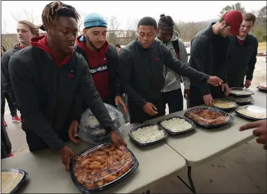  ?? NWA Democrat-Gazette/ANDY SHUPE ?? Mike Woods (from left), Isaiah Nichols and Devwah Whaley join other members of the University of Arkansas football team Thursday in serving a meal at the 7Hills Homeless Center’s day center in Fayettevil­le. Team members served food at several locations around Northwest Arkansas, including Arkansas Children’s Hospital Northwest, Mercy medical center in Rogers, and the Boys and Girls Club of Fayettevil­le.