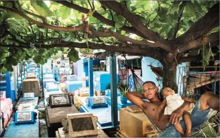  ?? ADAM DEAN/THE NEW YORK TIMES ?? A man rests with his granddaugh­ter in a hammock strung up over a tomb next to where he lives, at Manila North Cemetery in the Philippine­s, on April 19.