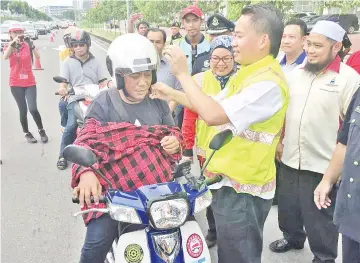  ??  ?? Peter presenting a helmet to one of the motorcycli­sts during the road safety awareness campaign at the city centre yesterday.