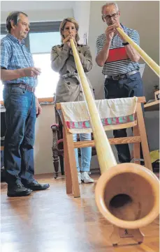  ?? FOTO: PAULINA STUMM ?? Alfons Neumann (links) und Franz Schoch versuchen Redakteuri­n Karin Kiesel das Alphornspi­elen zu zeigen.