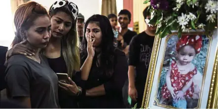  ??  ?? Jiranuch Trirat (left), 22, is comforted by friends as she looks at a photograph of her 11-month-old daughter Natalie during the last funeral rites at a temple in Phuket on April 29, 2017. Tearful relatives gathered outside a Thai temple to bury the...