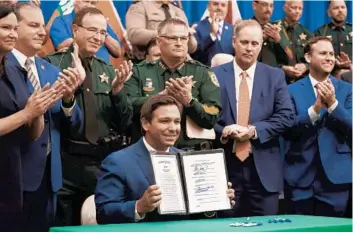  ?? RICARDO RAMIREZ BUXEDA/ORLANDO SENTINEL ?? Gov. Ron DeSantis holds the“anti-riot”bill he signed Monday at the Polk County Sheriff’s Office, surrounded by law enforcemen­t and legislator­s. The measure increases police powers to crack down on civil unrest.