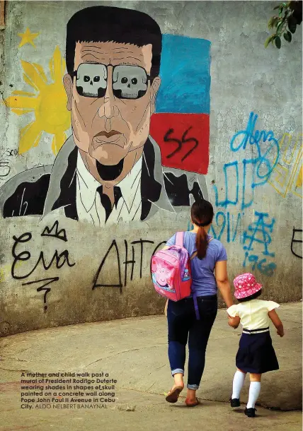  ?? ALDO NELBERT BANAYNAL ?? A mother and child walk past a mural of President Rodrigo Duterte wearing shades in shapes of skull painted on a concrete wall along Pope John Paul II Avenue in Cebu City.