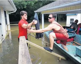  ?? Joe Raedle Getty Images ?? DISPLACED RESIDENT Collan Ortego, left, gets Jason Fatherree’s help retrieving a television set from his family’s flooded home in Sorrento, La.