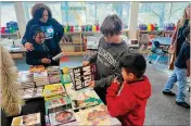  ?? H.M. CAULEY FOR THE AJC ?? William Pennington (center) volunteere­d to help Boyd Elementary students pick out books to take home during a December book fair.