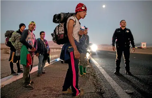  ?? AP ?? A police officer helps Central American migrants get a ride on trucks going from Mexicali to Tijuana yesterday.