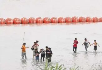  ?? Jerry Lara/Staff photograph­er ?? With buoys in the background, migrants traverse the U.S. side of the Rio Grande. This latest aspect of Operation Lone Star doesn’t cast a humanitari­an light on migrants because that would demonstrat­e the need for comprehens­ive reform.