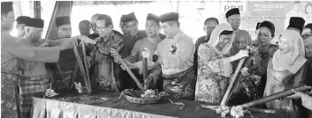  ??  ?? Awang Tengah (fourth right) opening the ‘lemang’ inside the bamboo to mark the Hari Raya Aidilfitri celebratio­n. Lee is at fourth left.