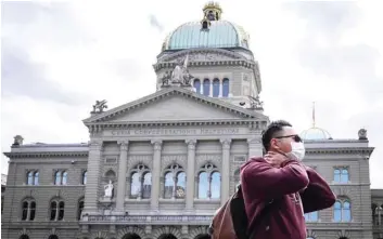  ?? — AFP ?? A man wearing a mask walks past the Swiss House of Parliament in Bern.