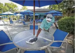  ?? Steve Gonzales / Staff photograph­er ?? Restaurant server Clyde Tugwell sanitizes a table at The Cool Water Cafe near the Lazy River in The Woodlands Resort.